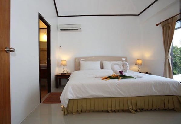 Habitación de hotel con una cama grande, dos lámparas de noche, un equipo de aire acondicionado y vistas a zonas verdes.