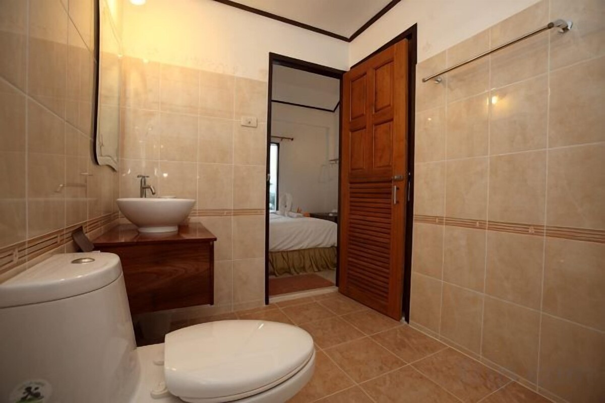 A bathroom with a toilet, sink, and wooden door leading to a bedroom.
