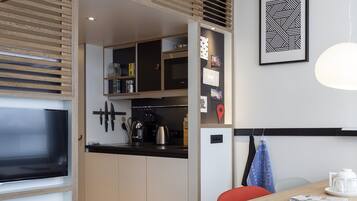 A modern kitchen with wooden cabinetry, a built-in TV, and a dining area with a red chair and a table.