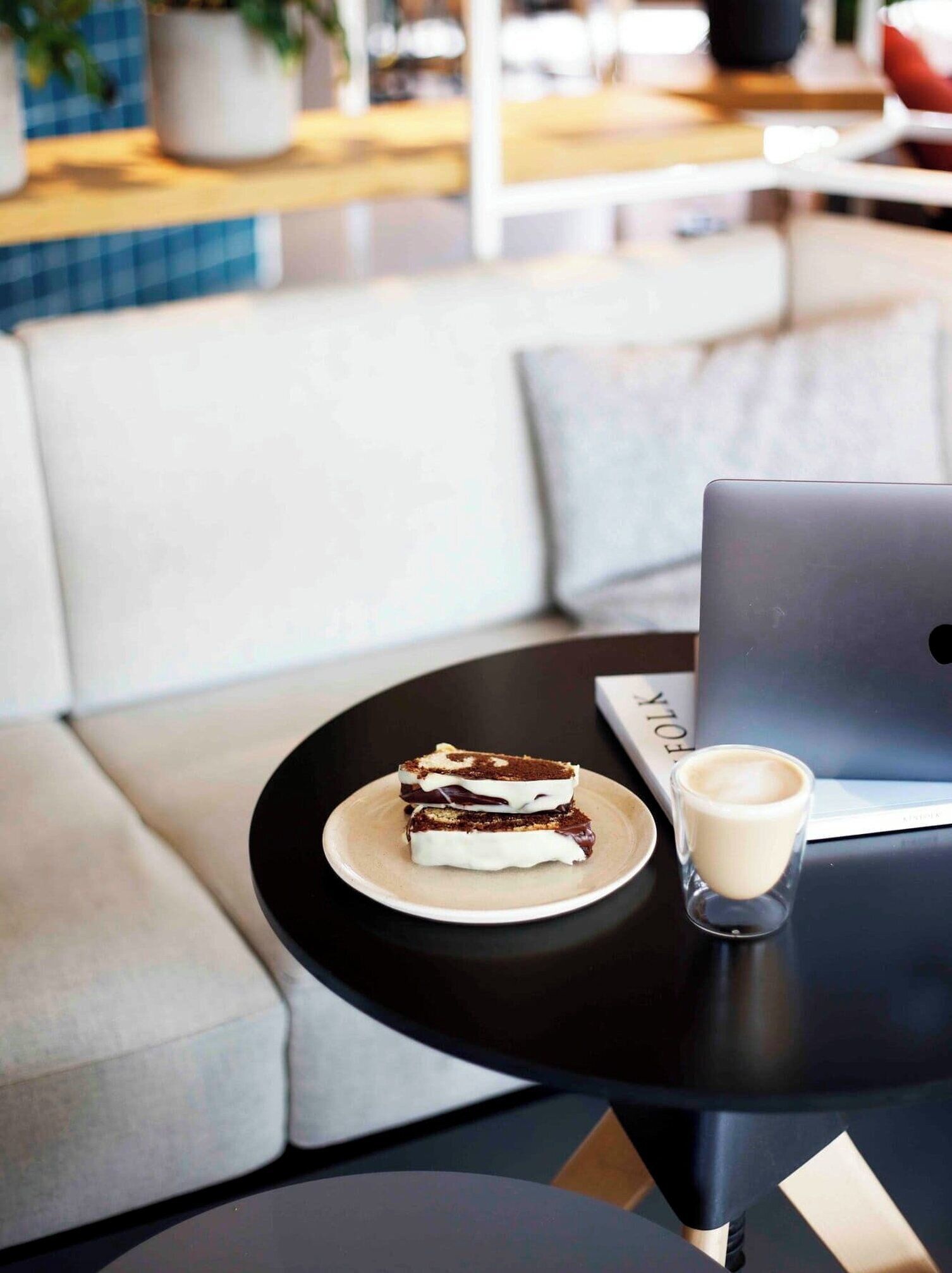 A laptop on a table with a plate of dessert and a glass of milk.