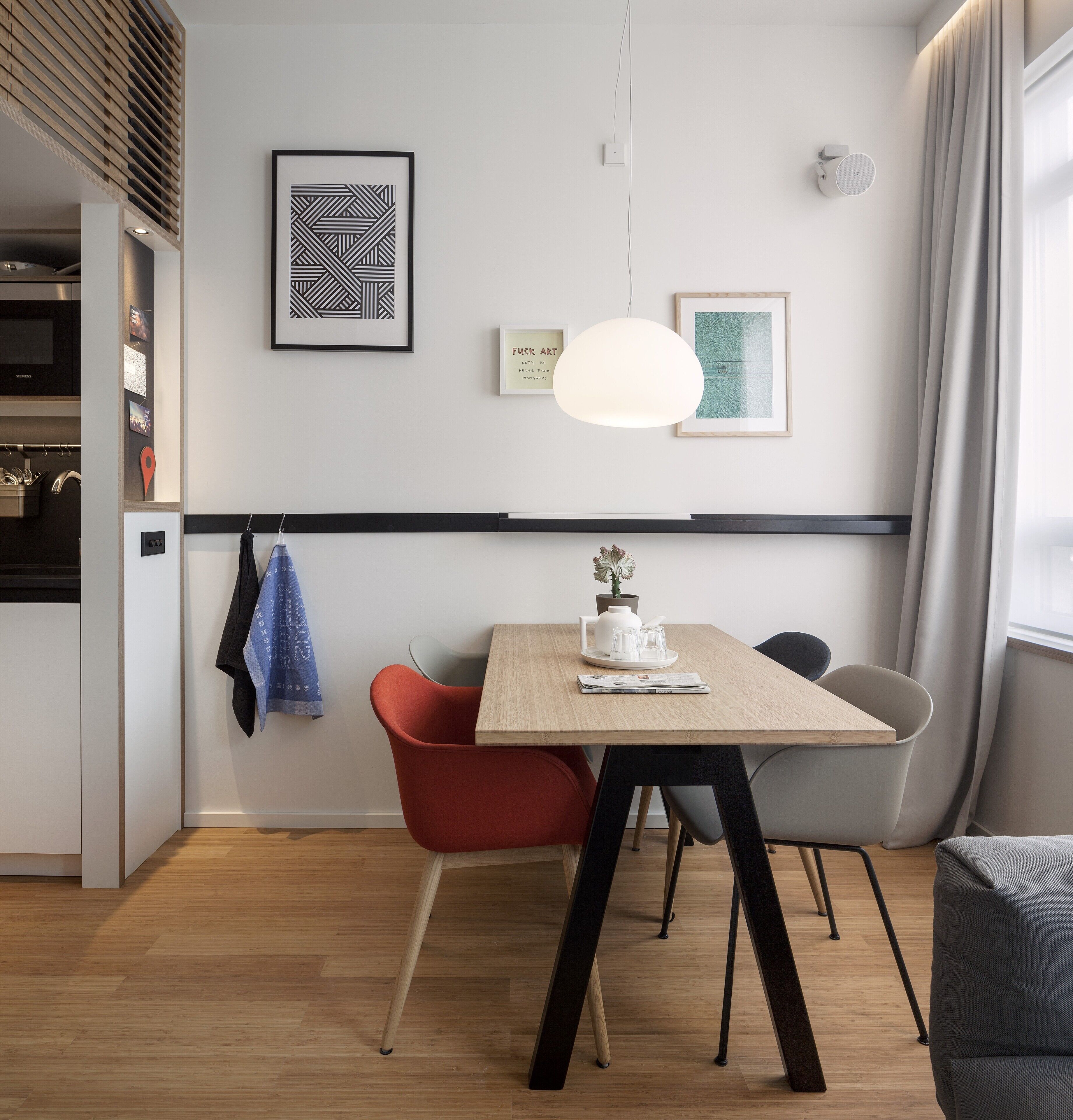 A modern dining area with a wooden table, red and grey chairs, a white pendant light, and artwork on the walls.