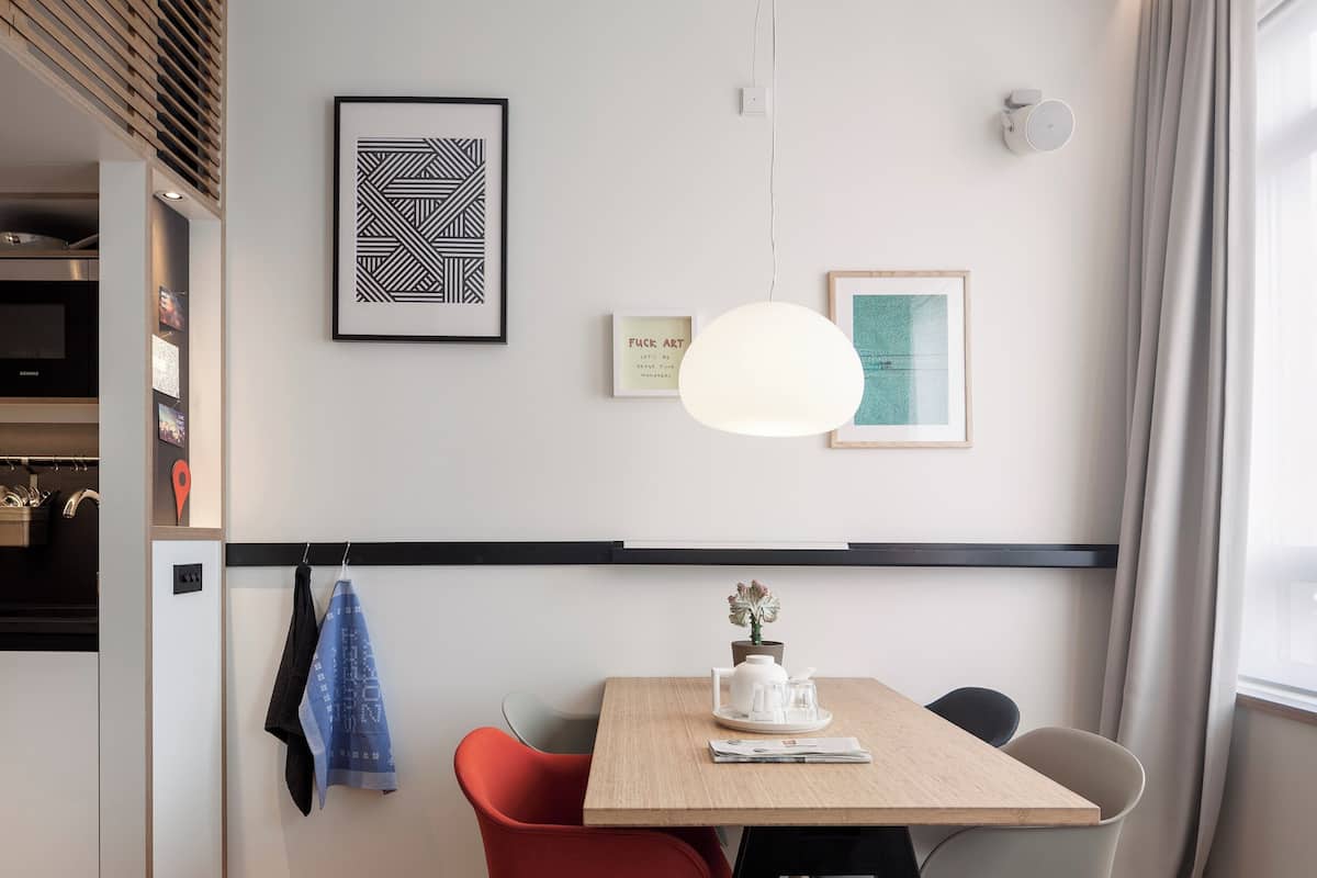 Un comedor moderno con una mesa de madera, sillas rojas y grises, una lámpara colgante blanca y obras de arte en las paredes.