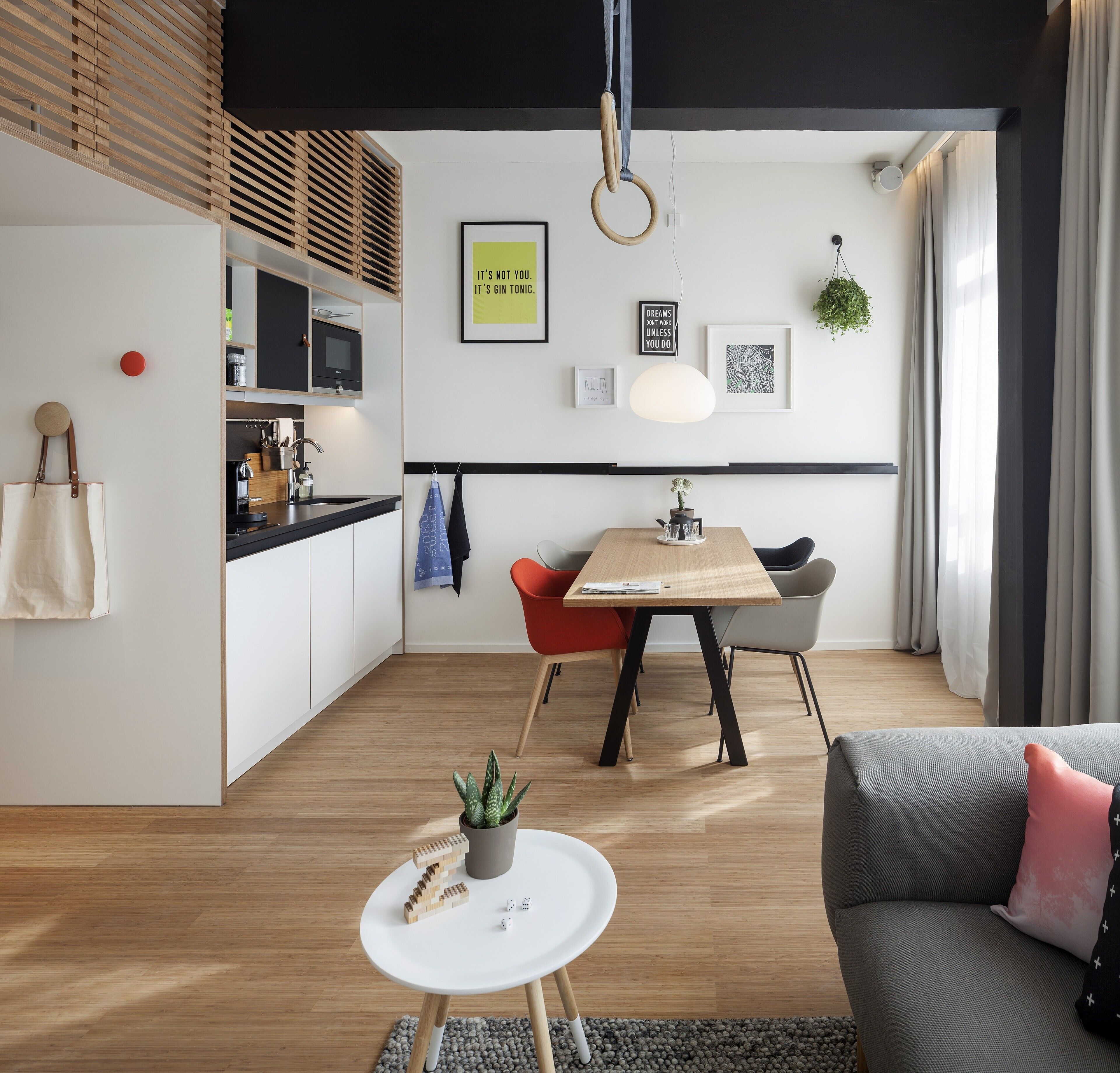 Eine moderne Küche mit Holzboden, ein Essbereich mit Holztisch und -stühlen sowie ein Wohnbereich mit Sofa und Couchtisch.