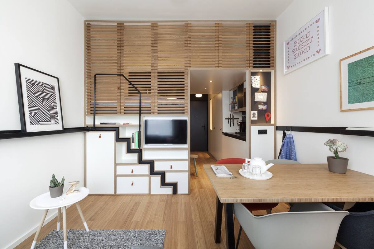 Una sala de estar moderna con televisor, pared de listones de madera y comedor con mesa y sillas.