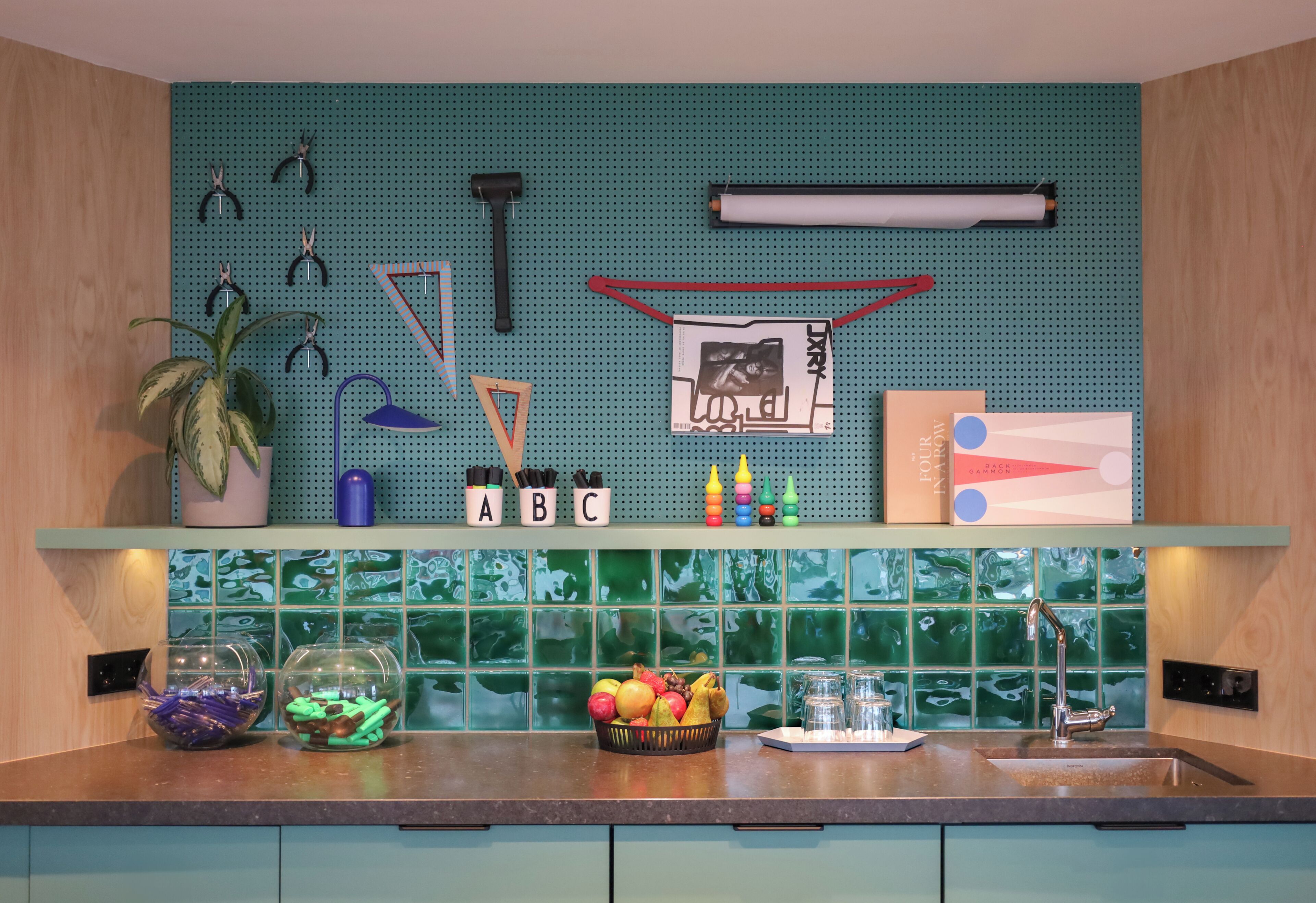 A kitchen with a pegboard wall, a fruit bowl, a sink, and a potted plant.
