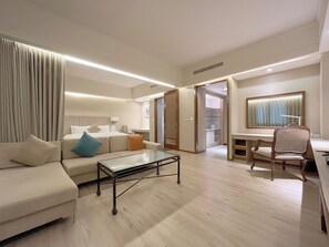 Une chambre d’hôtel moderne équipée d’un canapé, d’une table basse en verre, d’un bureau avec une chaise et d’un dressing.