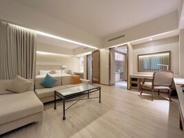 Une chambre d’hôtel moderne équipée d’un canapé, d’une table basse en verre, d’un bureau avec une chaise et d’un dressing.