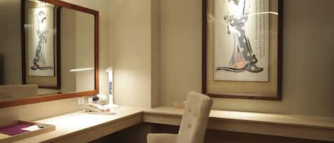 Ein Hotelzimmer mit einem großen Spiegel, einem gerahmten Kunstwerk an der Wand, einem Schreibtisch mit Telefon und einem Sessel.