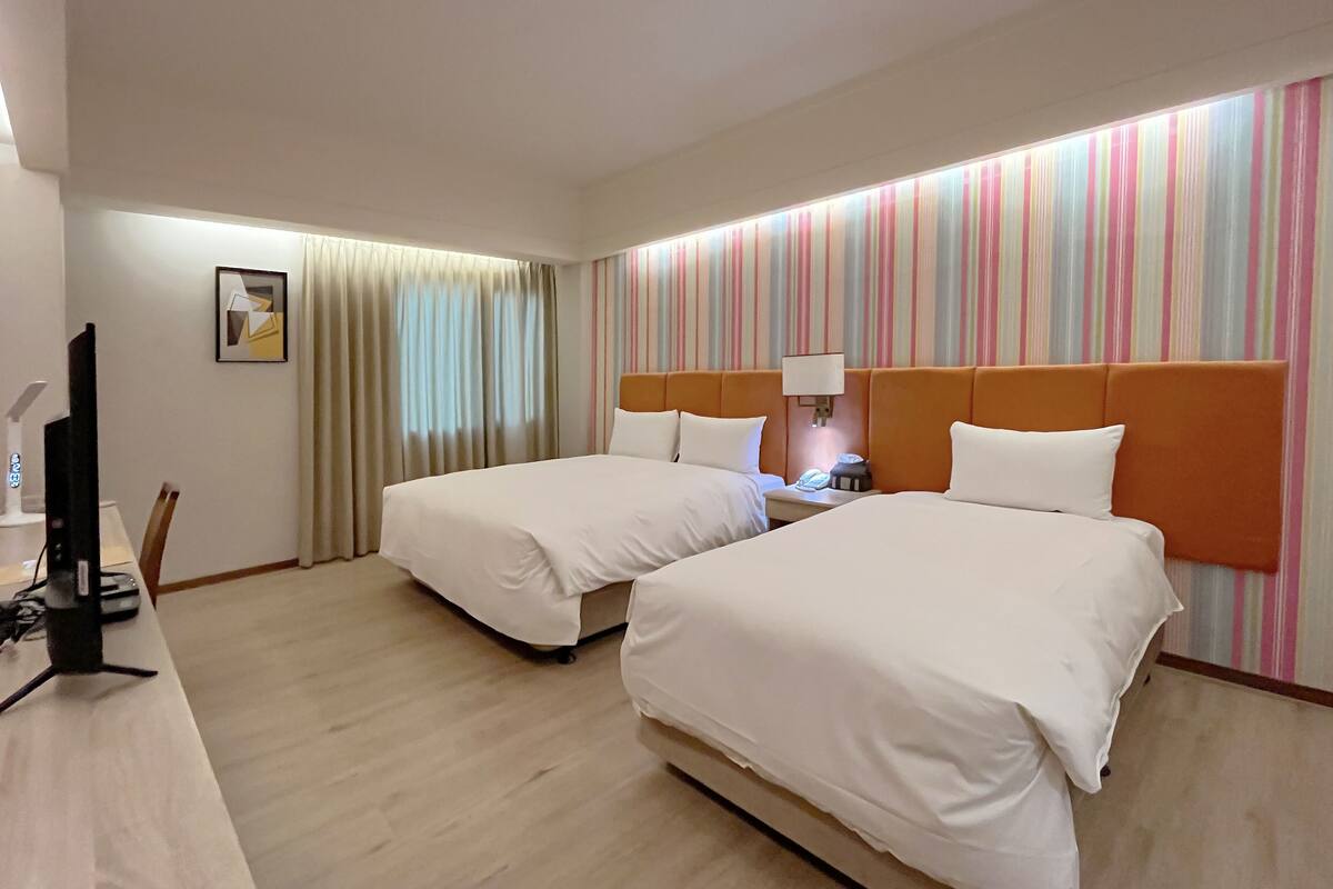 Habitación de hotel con dos camas, un escritorio con computadora, una lámpara y un muro a rayas.