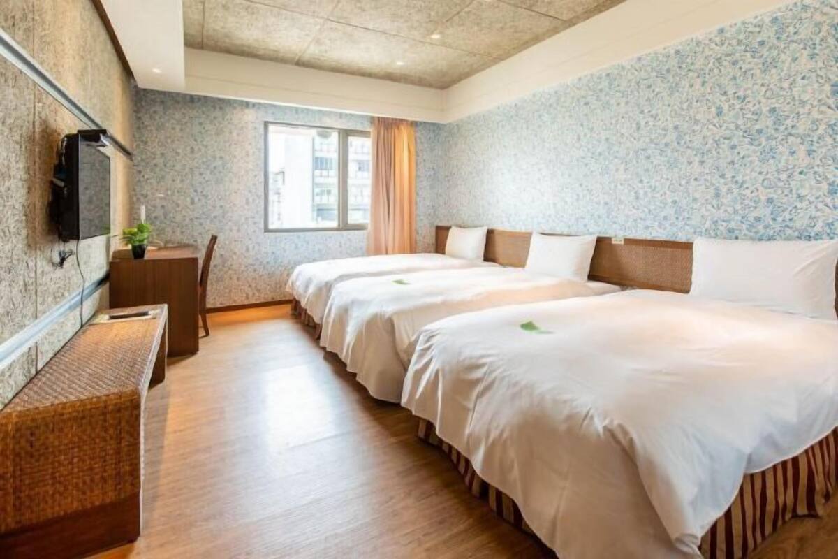 Habitación de hotel con dos camas, un escritorio, un televisor y una ventana con vista a edificios.