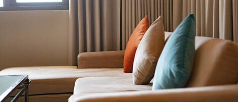 Una sala de estar moderna con un sofá color beige, una mesita y una ventana con cortinas.