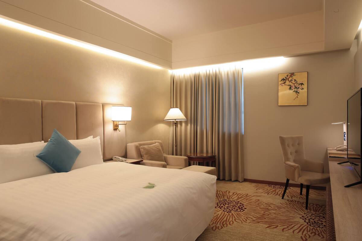 Habitación de hotel con una cama grande, un escritorio, una silla, una lámpara y un cuadro en la pared.
