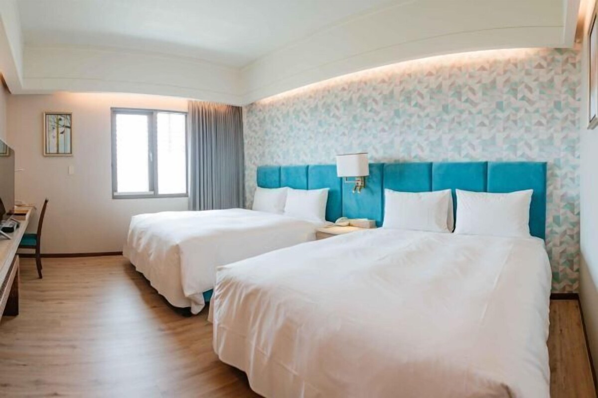 A hotel room with two beds, a desk, and a chair.