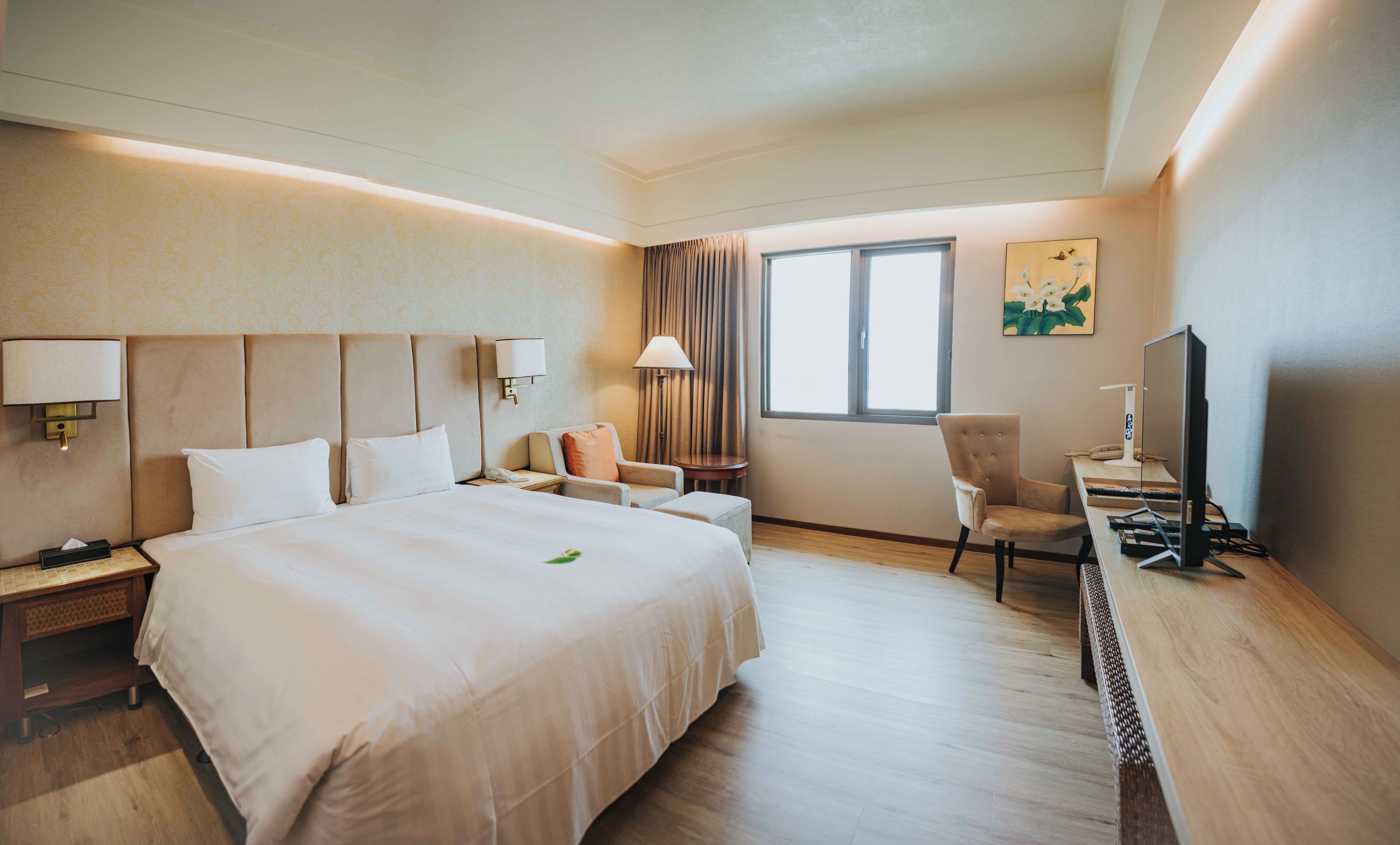 Habitación de hotel con una cama grande, un escritorio con computadora, una silla y una ventana con cortinas.