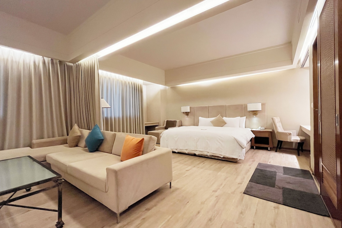 A hotel room with a bed, a sofa, a small table, and a desk with a chair.