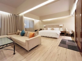 A hotel room with a bed, a sofa, a small table, and a desk with a chair.