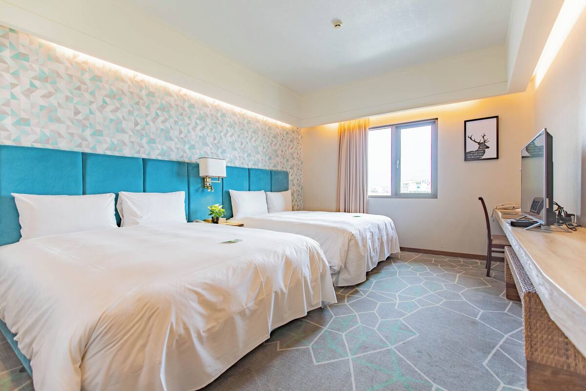 Habitación de hotel con dos camas, un escritorio, una silla, un televisor y una ventana con cortinas.