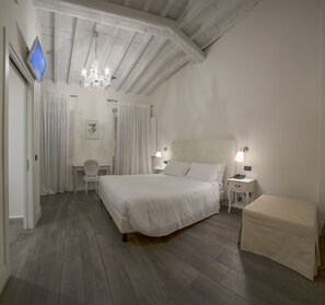 Ein Schlafzimmer mit einem großen Bett, einem Schreibtisch, einem Sessel, einem Fernseher und einer Kandelaber.