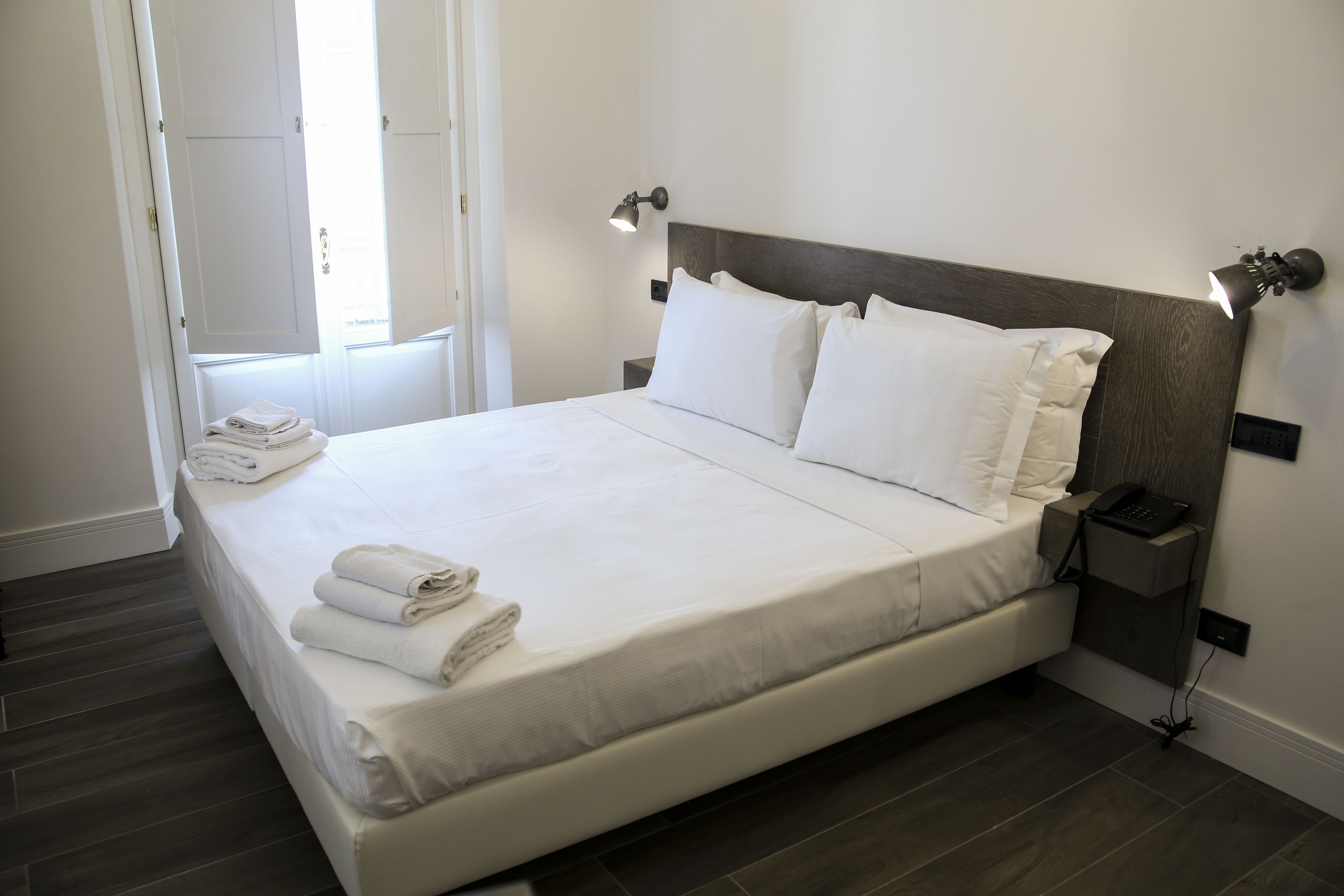 A neatly made bed with white linens and pillows, a bedside lamp, and a folded towel on the nightstand.