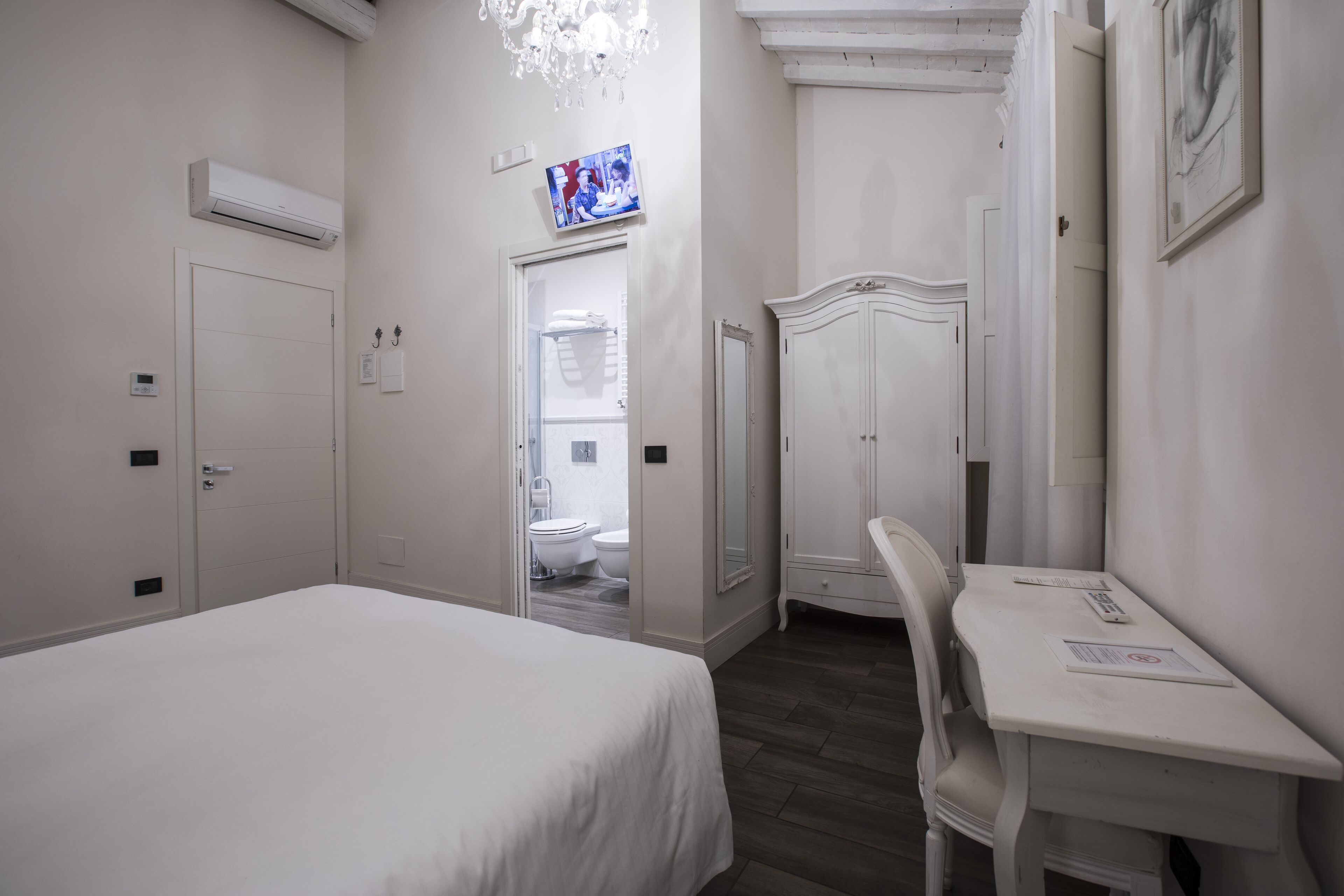 Habitación de hotel con cama, escritorio, silla, armario, televisor y baño visible a través de una puerta abierta.