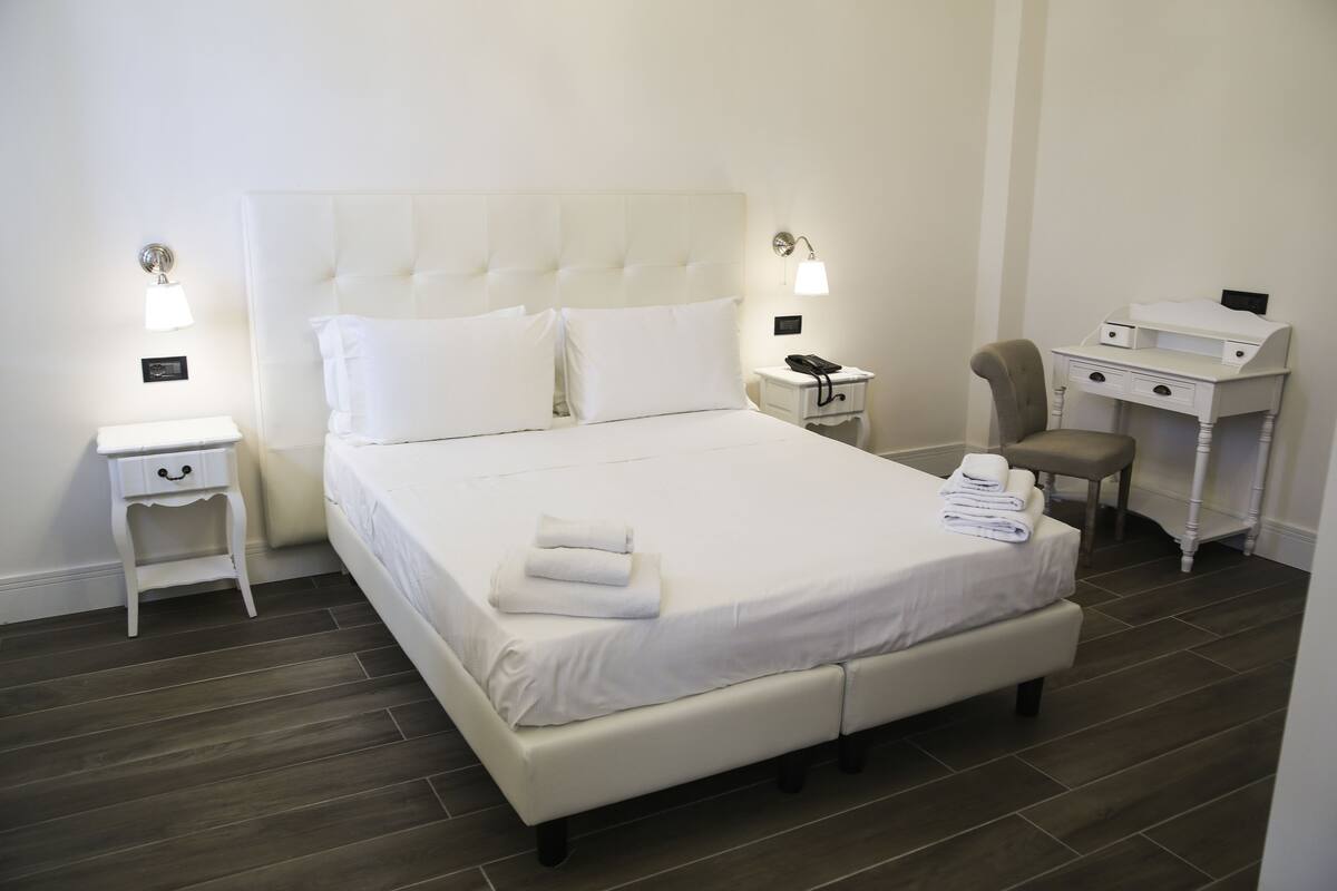 A neatly arranged hotel room with a large bed, bedside tables, a desk, and a chair.