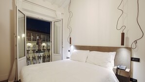 Ett hotellrum med en stor säng, ett nattduksbord med en telefon, en väggmonterad lampa och ett fönster med utsikt över byggnaderna utanför.