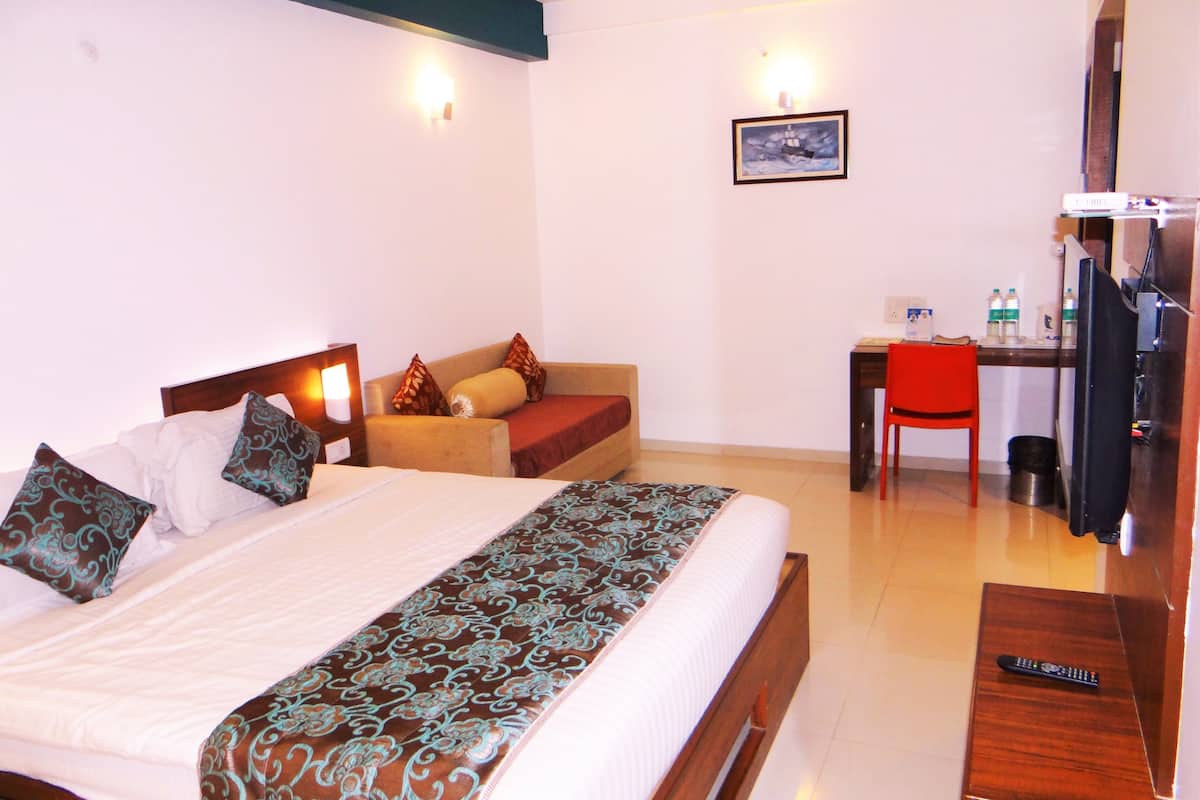 A hotel room with a bed, a desk, a chair, a television, and a refrigerator.