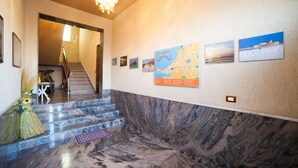 A hallway with a marble floor, a staircase, and a wall decorated with framed pictures and a map. - B&B Il Cavaliere (Trapani)