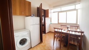 A compact kitchen with wooden cabinets, a built-in washing machine, a dining table with chairs, and a window providing natural light. - B&B Il Cavaliere (Trapani)