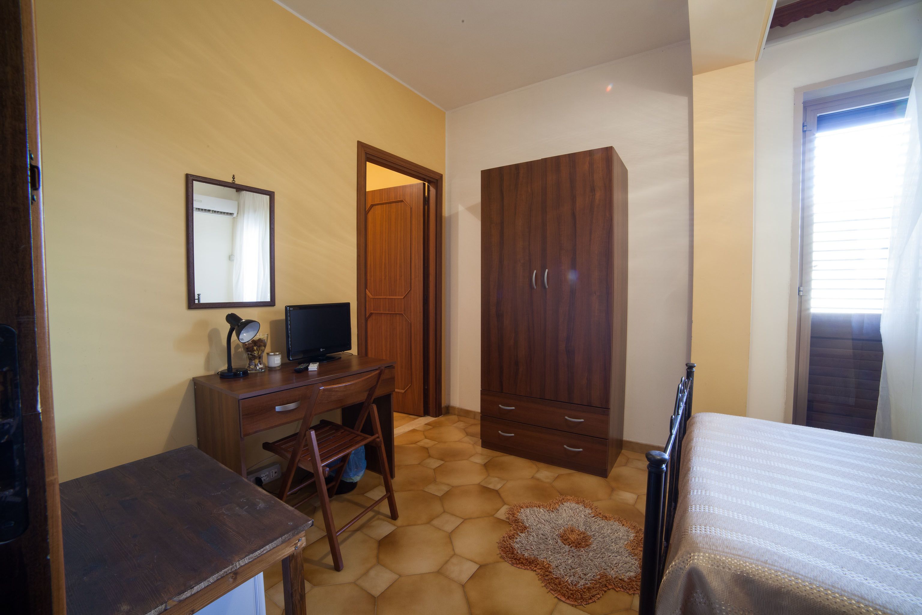 A bedroom with a wooden desk, a television, a wardrobe, and a bed.