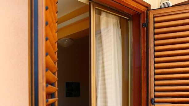 A room with a bed, a window with a curtain, and a wooden door with louvered panels. - B&B Il Cavaliere (Trapani)