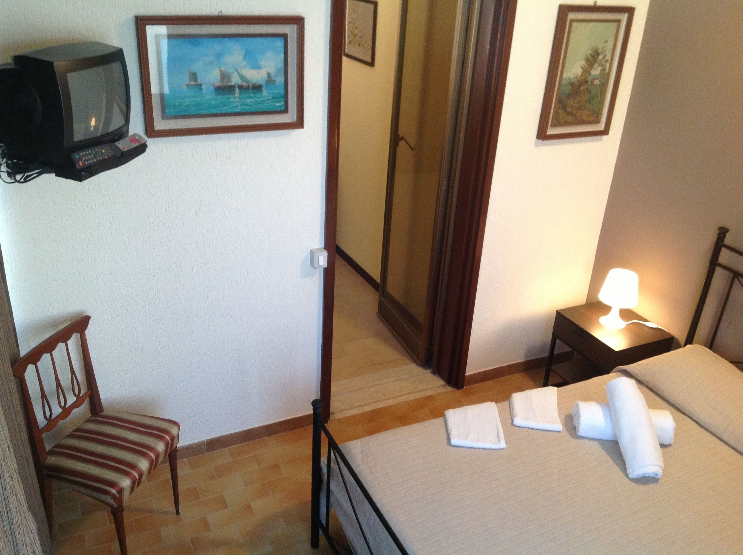 A hotel room with a bed, a chair, a TV, a mirror, and a nightstand with a lamp.