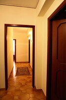 A hallway with a wooden door on the right, a rug on the floor, and a light fixture on the wall.