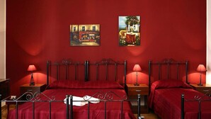 A room with a red wall, two beds with red bedding, and two bedside tables with lamps. There are two paintings on the wall. - B&B Il Cavaliere (Trapani)