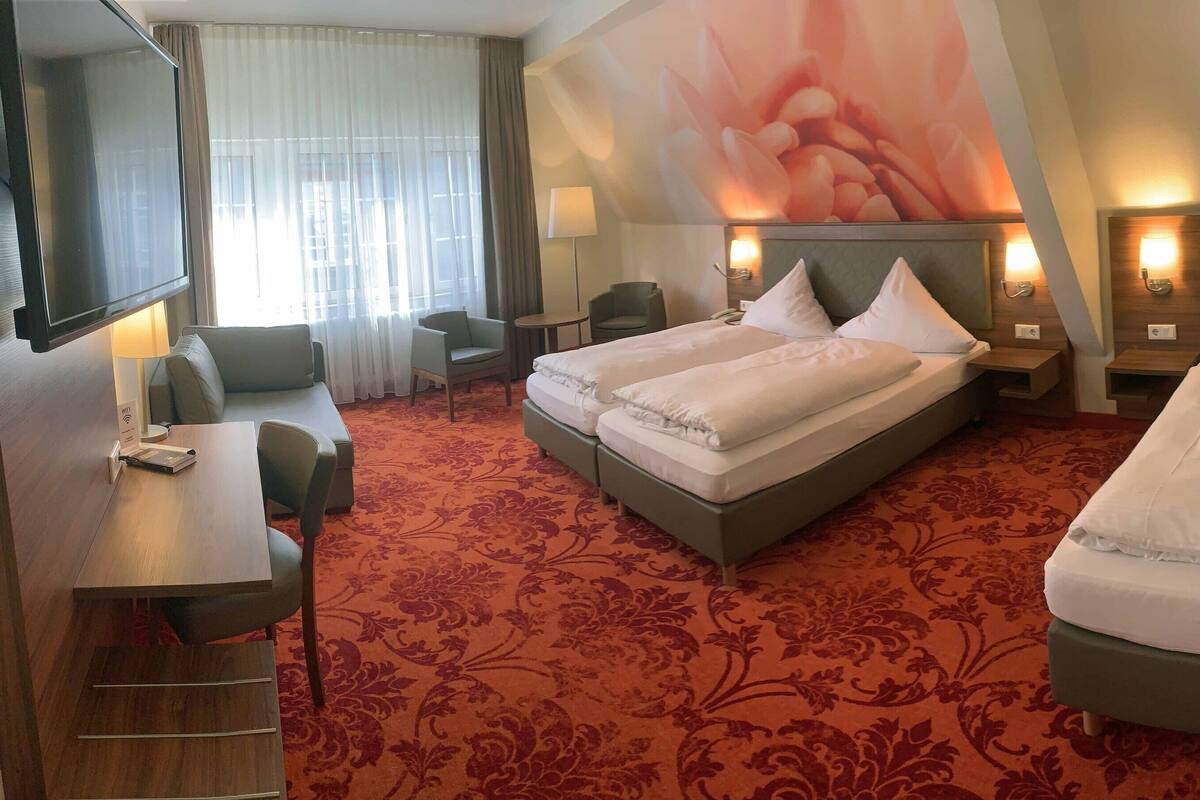 Une chambre d’hôtel avec un grand lit, un bureau, une chaise, une télévision et une grande œuvre d’art florale accrochée au mur.