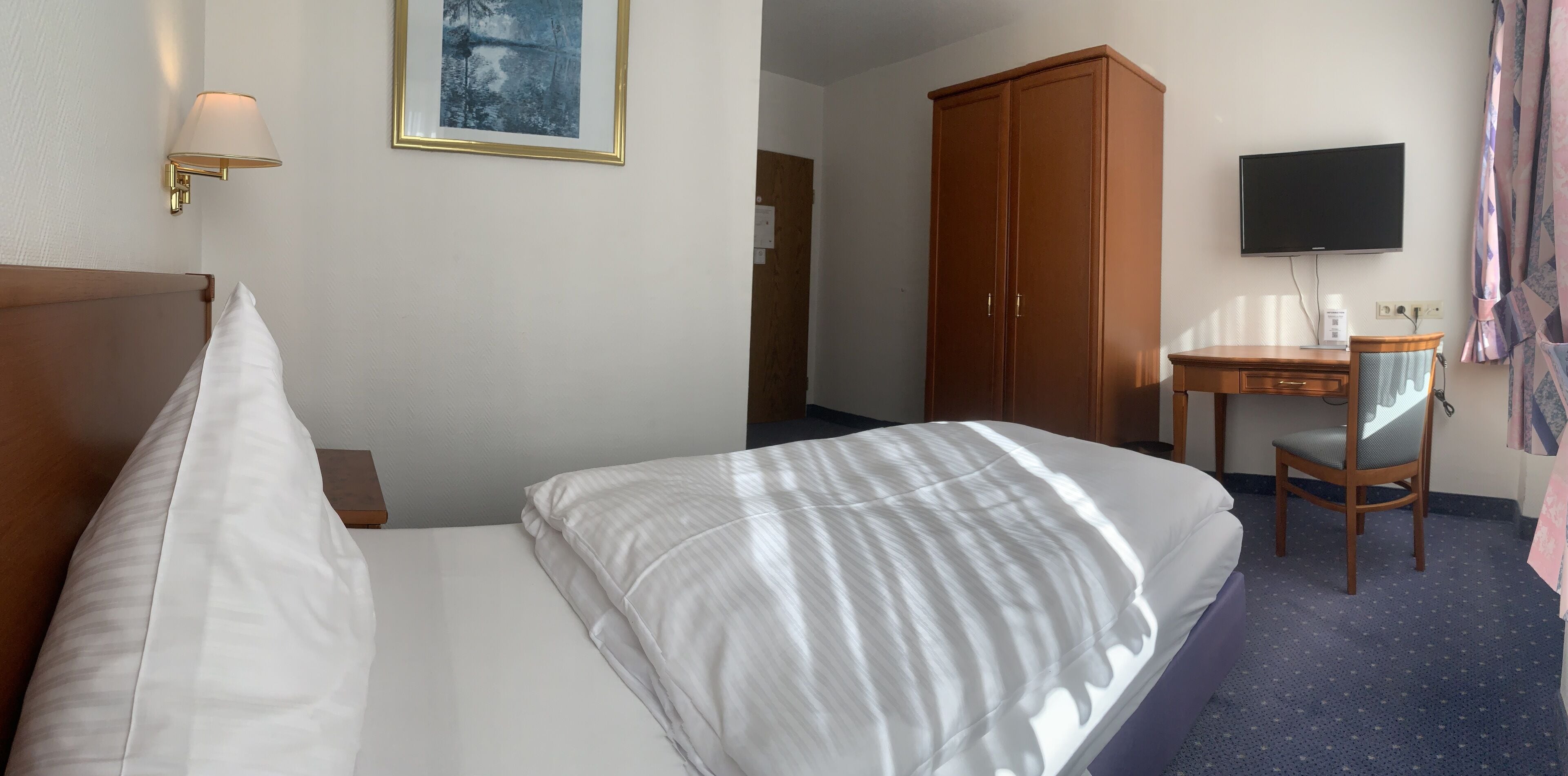 Una habitación de hotel con cama, escritorio, silla, televisor y armario.