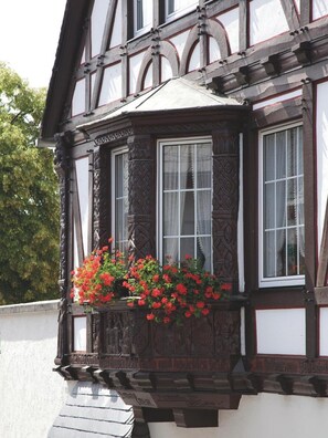 A half-timbered building with a bay window featuring red flowers.
