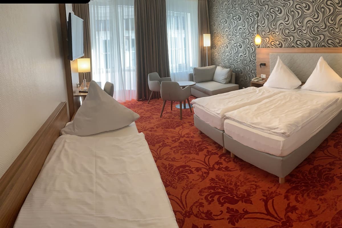 Une chambre d’hôtel avec deux lits simples, un canapé, une petite table et un téléviseur.