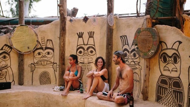A group of people sitting on a stone bench against a wall with tribal artwork. - Tiberias Hostel (Tiberias)