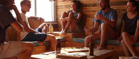 A group of people sitting on wooden benches in a rustic room with a wooden wall and a window.