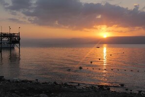 A sunset over a calm body of water with a pier on the left. - Tiberias Hostel (Tiberias)