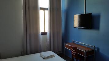 A room with a bed, a desk, a chair, a television mounted on the wall, and a window with curtains.