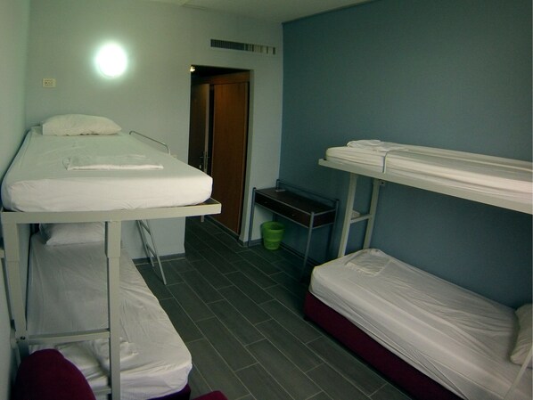 A dormitory room with bunk beds, a small table, and a trash bin. - Tiberias Hostel (Tiberias)
