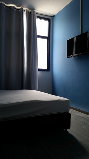 A bedroom with a bed, a window with curtains, and a TV mounted on the wall. - Tiberias Hostel (Tiberias)