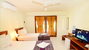Habitación de hotel con dos camas, televisión, refrigerador pequeño y ventilador de techo.