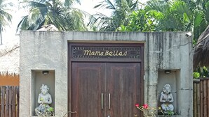 Una puerta de madera con la inscripción "Mama Bellas" en la parte superior, flanqueada por dos pequeñas estatuas.