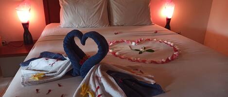 A neatly made bed with a heart-shaped towel arrangement, a flower garland, and a note on the bed.