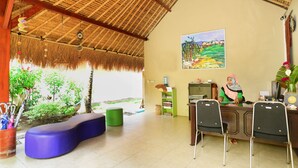 Una habitación con techo de paja, un cuadro en la pared, un escritorio con sillas y un banco verde.