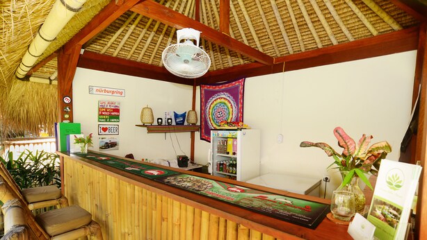 A reception area with a bamboo reception desk, a fan, and a colorful wall hanging. - Mama Bella's Retreat (Senggigi)