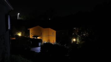 A house with a yellow facade, surrounded by greenery, and illuminated by multiple lights.